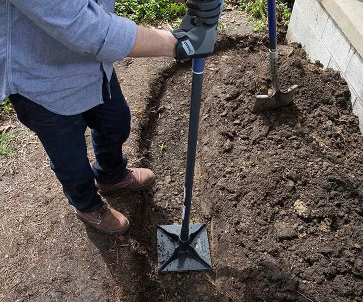 Person using a hand tamper to compact soil