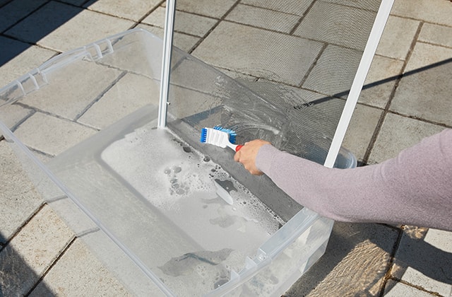 Person cleaning a screen in a tub of soapy water