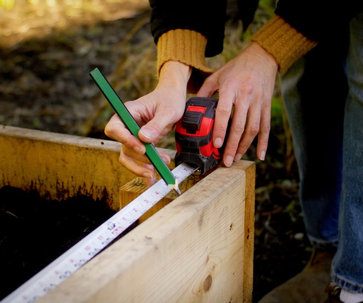 Woman measuring a wooden raised bed