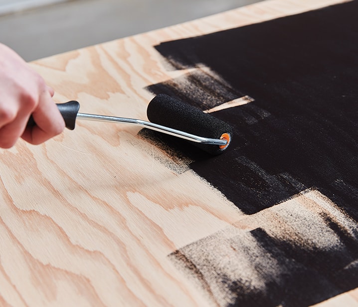 Woman painting a sheet of plywood black