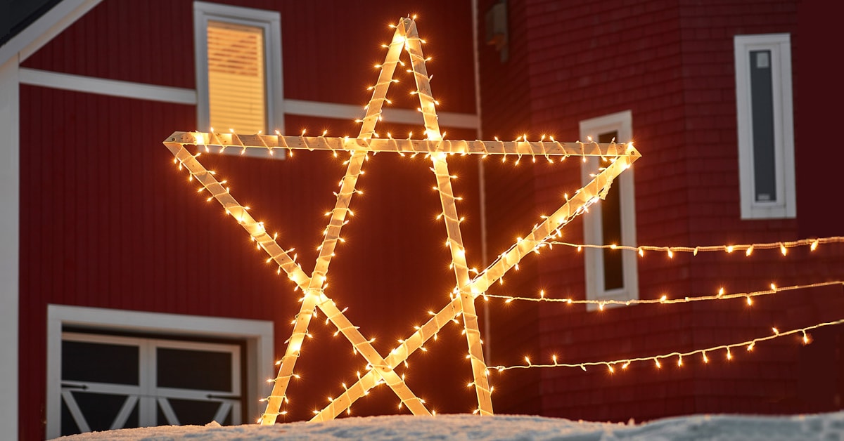 Étoile filante en bois illuminée devant une maison