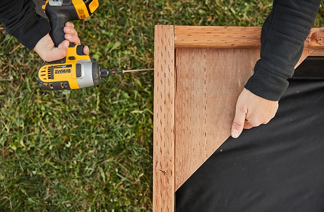 Person adding corner benches to a wooden sandbox