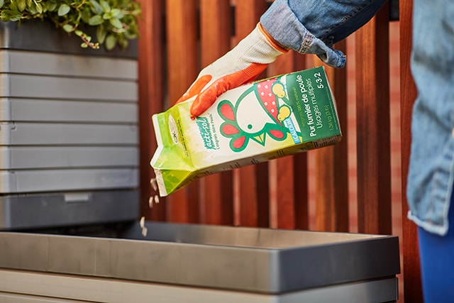 Personne versant du fumier de poule dans une jardinière